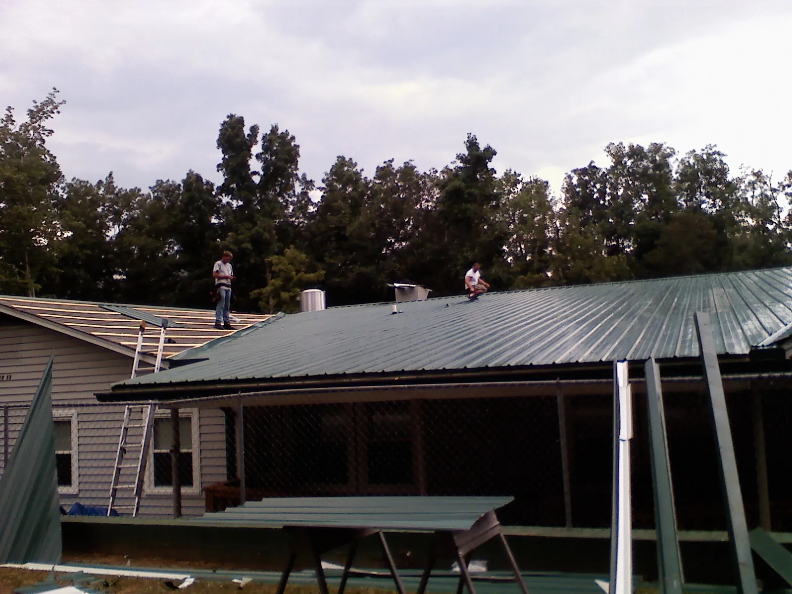 Two roofers installing green metal panels above a covered porch in Richmond